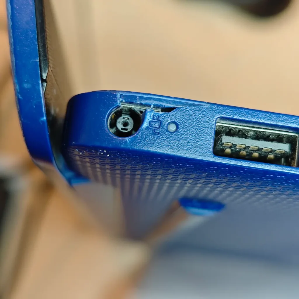 Fizički oštećen konektor za punjenje i polomljena plastika oko porta na plavom polovnom laptopu